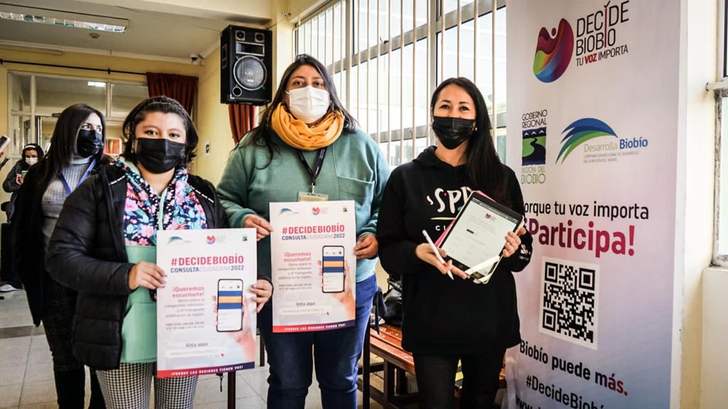 Tres mujeres sosteniendo carteles de consulta Decide Biobío en votación electrónica con EVoting